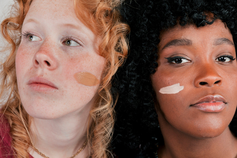 Deux femmes côte à côte, l’une à la peau claire avec des taches de rousseur et des cheveux roux bouclés, l’autre à la peau foncée avec des cheveux noirs bouclés.