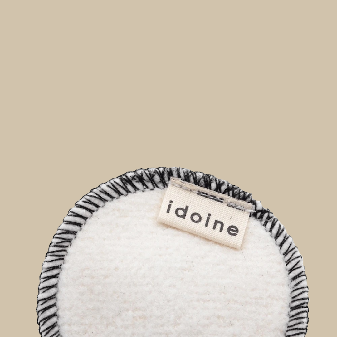 Idoine Bio reusable cleansing pad made of soft fabric with black stitched edges and a beige tag, designed for gentle and eco-friendly skincare routines.