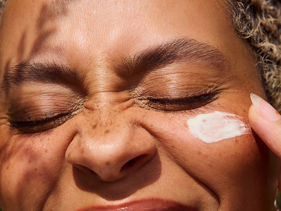 Gros plan d’une femme appliquant une crème visage sous l’œil, peau texturée au soleil, expression concentrée illustrant un soin doux et ciblé.