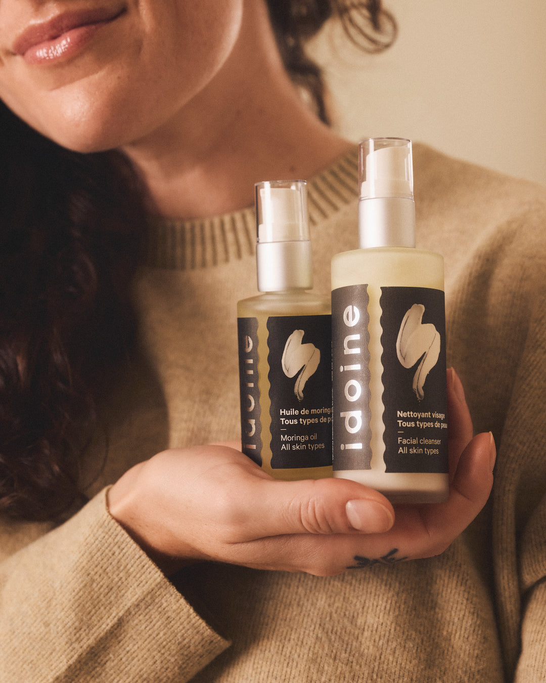 Woman holding Idoine organic moringa oil and facial cleanser in frosted glass pump bottles, natural vegan skincare for all skin types