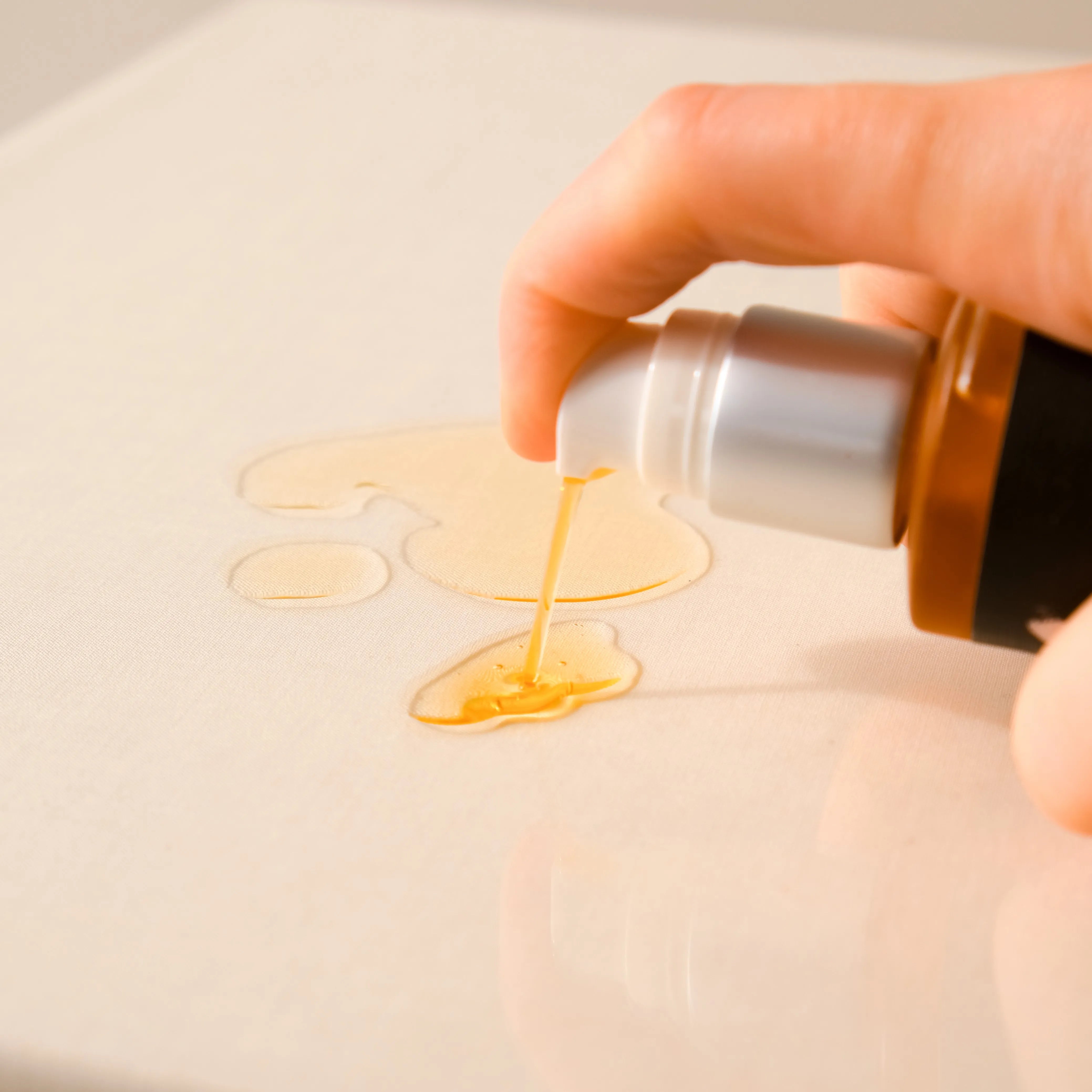 Hand pressing a pump bottle to dispense a small amount of oil onto a smooth surface in a close-up shot.