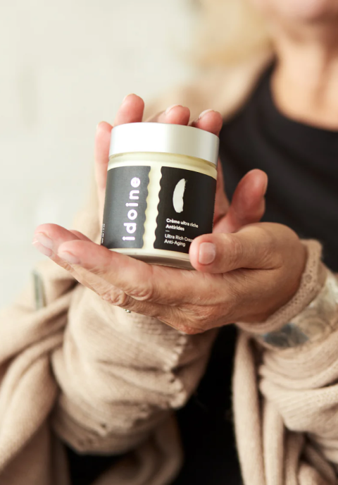 Une femme tenant un pot de crème anti-âge ultra riche pour le visage Idoine dans ses mains.