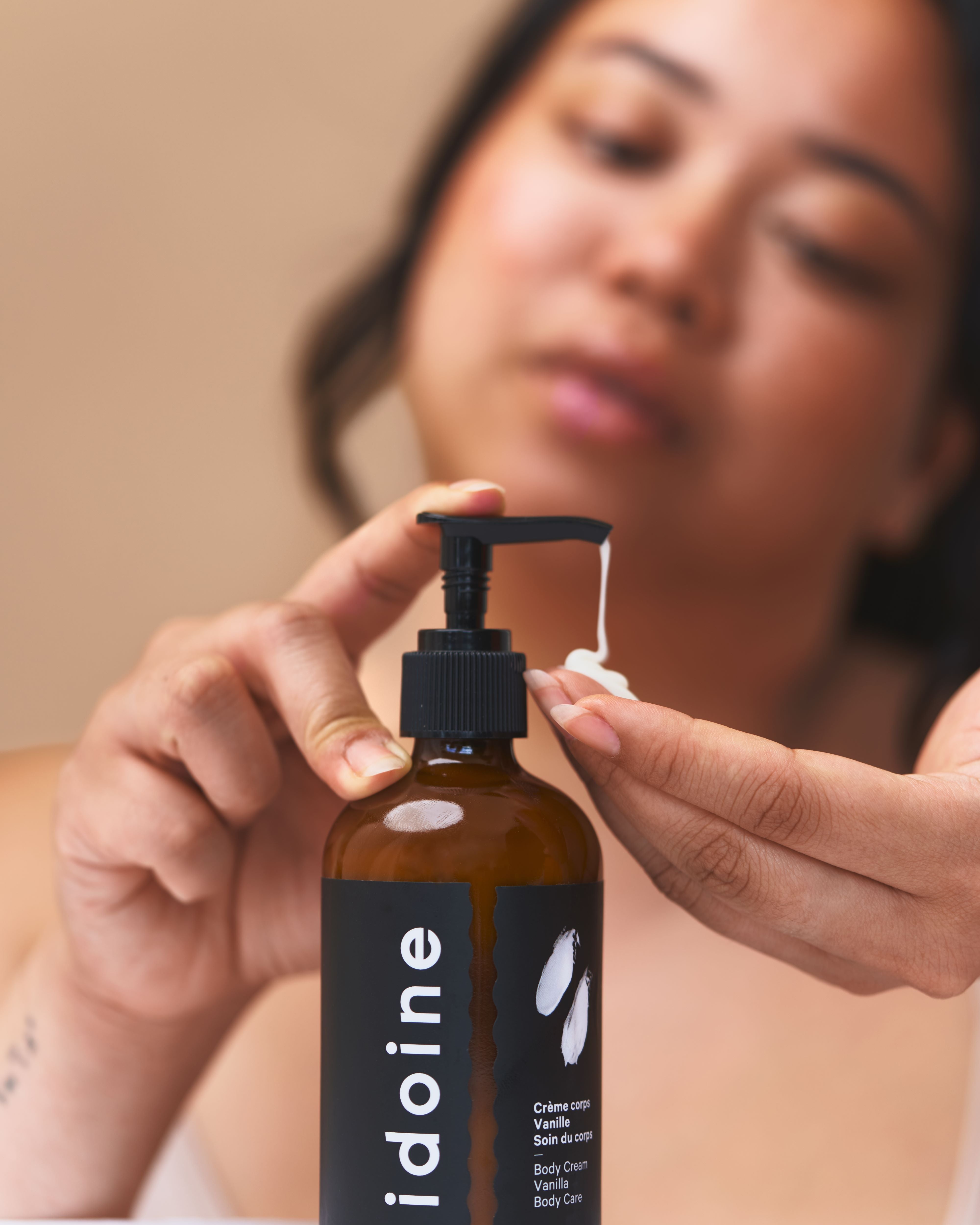Woman applying Idoine organic vanilla body cream from an amber pump bottle, natural moisturizing skincare for soft and nourished skin