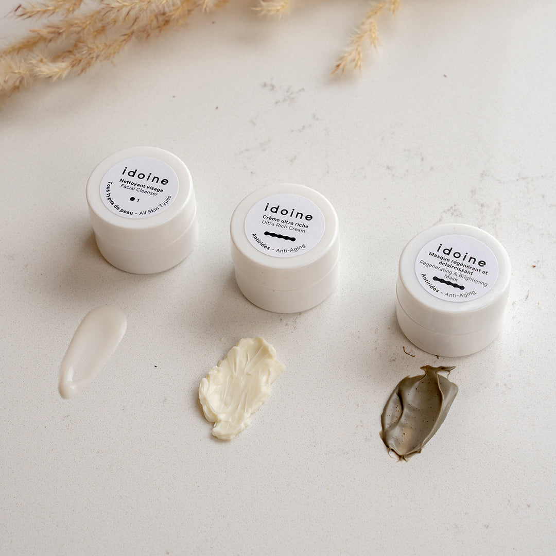 Idoine organic skincare mini trial set with three sample jars—facial cleanser, ultra rich anti-aging cream, and regenerating face mask—shown with textures on a white surface