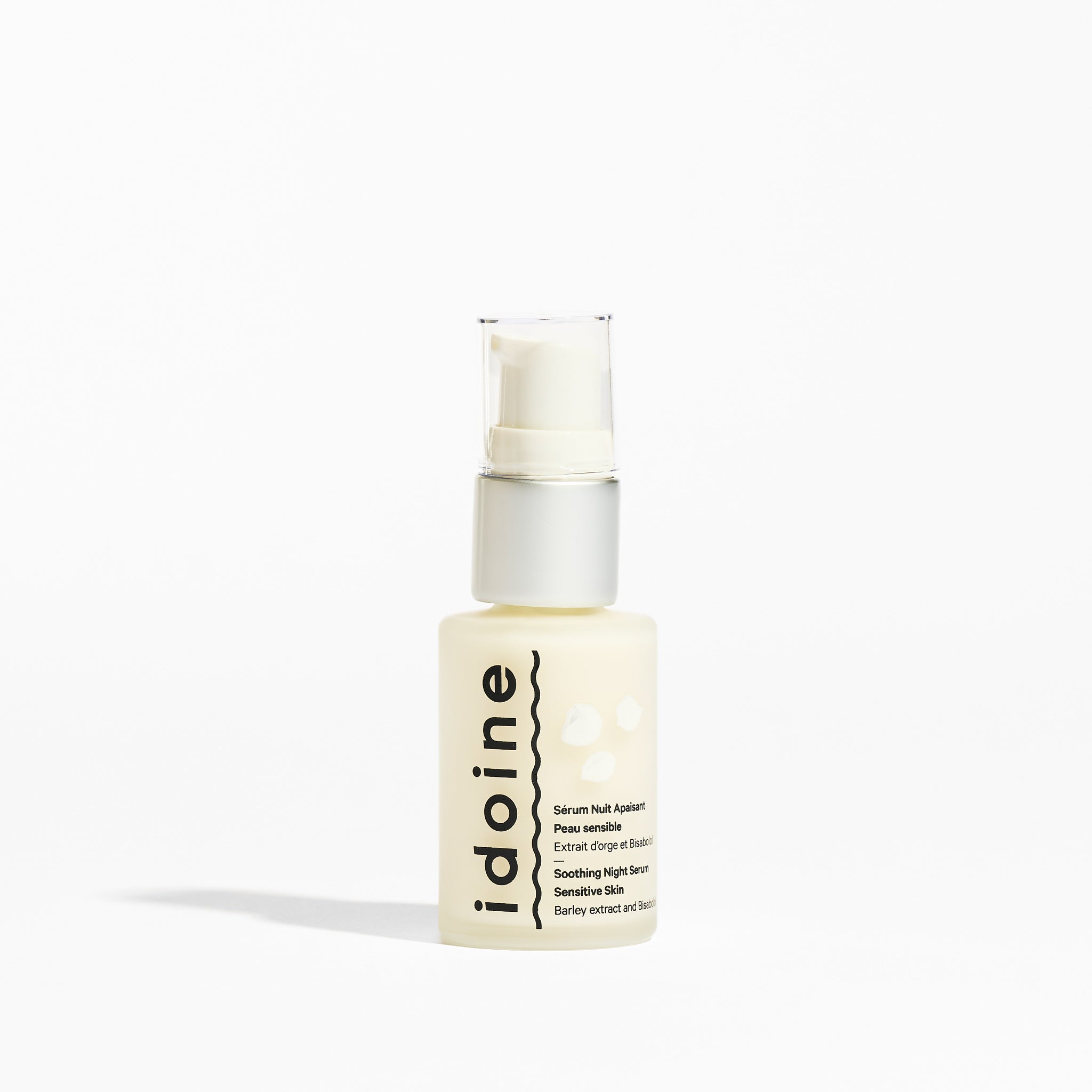 Flacon produit Flacon pompe du sérum apaisant Idoine Bio pour peau sensible en verre translucide, étiquette bilingue, fond blanc minimaliste épuré.