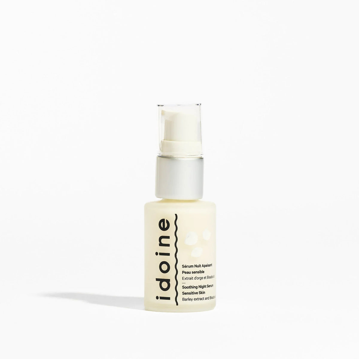  Flacon pompe en verre translucide d’un sérum visage antirides Idoine Bio, fond blanc minimaliste, gamme de soins ciblés antirides